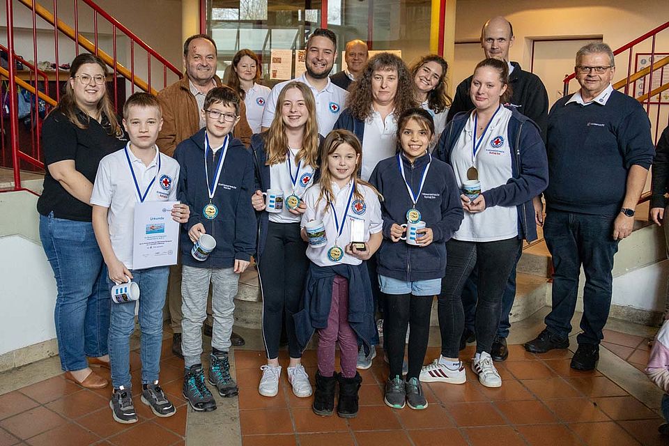 Die Sieger der Stufe 1 von der Wasserwacht Pfarrkirchen: Raphael Wernitz, Maria Lindinger, Paula Posset, Lena Maier, Ferdinand Lindinger (Trainerin: Sophie Knopp). Zusätzliche Personen auf dem Bild: 1 v.l. Julia Gschwandtner (Leiterin JRK Arnstorf), 3 v.l. Christian Thiel (1. Bürgermeister Massing), 4 v.l. Verena Grad (Jugendleiterin Wasserwacht Berzirksverband Niederbayern/Oberpfalz), 5 v.l. Benjamin Taitsch (1 stv. Vorsitzender Wasserwacht Bayern), 6 v.l. Josef Feigl (1. Stv. Vorsitzender Kreiswasserwacht Rottal-Inn), 8 v.l. Maria Gruber (Jugendleiterin Kreiswasserwacht), 3 v.r. Andreas Rehrl (BRK Kreisgeschäftsführer Rottal-Inn), 1 v.r. Hans Nothaft (Vorsitzender Kreiswasserwacht & Bezirksvorsitzender Wasserwacht Niederbayern/Oberpfalz).